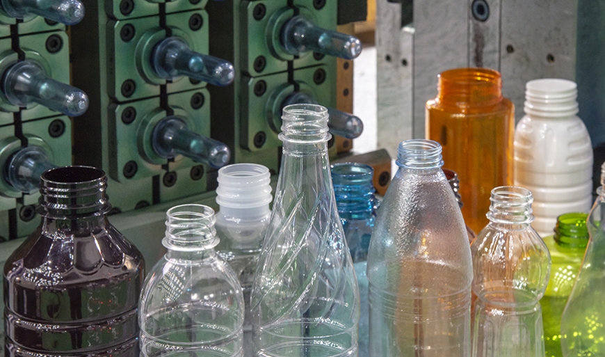 Close-up of PET plastic bottle manufacturing process showing molds and various transparent, colored, and textured plastic bottles.