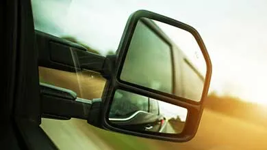 Close-up of a truck's split, black side-view mirror reflecting a trailer side and the road.