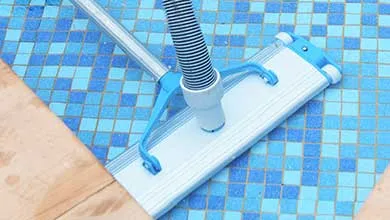 Close-up of a pool vacuum head cleaning a blue-tiled swimming pool bottom.