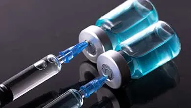 Two syringes draw bright blue liquid from two glass vials.