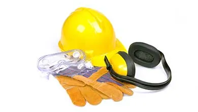 A yellow hard hat, safety goggles, work gloves, and ear defenders are neatly arranged on a white surface.