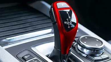 Close-up of an automatic car gear shifter with a red and black handle on the center console.