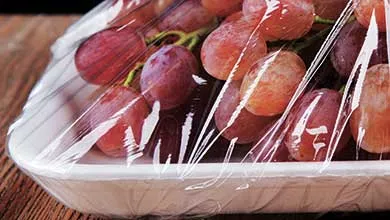 Close-up of a white container filled with red grapes, covered by clear plastic wrap.