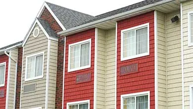 Low-angle view of a multi-story building with alternating tan horizontal siding and red shake siding on its exterior.