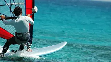 Windsurfer riding across clear blue water with a colorful sail, demonstrating lightweight composite performance.