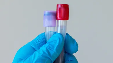 Gloved hand holding two capped laboratory sample tubes.