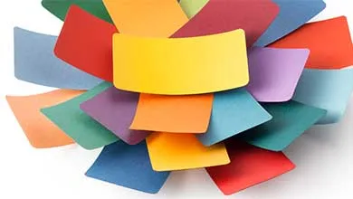 Colorful rectangular paper sheets arranged in a radial, flower-like pattern on a white background, with a yellow sheet at the center surrounded by red, orange, light blue, dark blue, purple, teal, and green sheets.