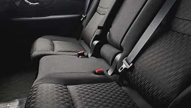 Interior view of dark fabric car back seats with a textured diamond pattern, showing seat belts and red buckle release buttons.