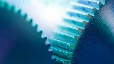 Close-up of two interlocking metal gears with cyan-blue metallic sheen, showing sharp, serrated edges against a softly blurred background.