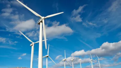 在晴朗的蓝天和分散的云朵下，风力发电机矗立在广阔的景观中。