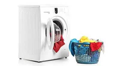 A white front-loading washing machine with its door open, showing a red garment inside, next to a blue laundry basket filled with red, yellow, and blue clothes.
