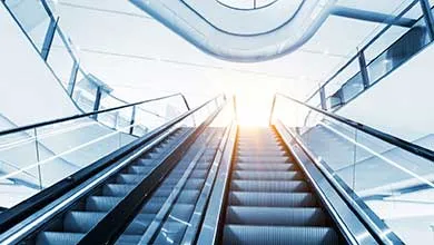 Low-angle view of two escalators in a modern building, with bright light shining from above.