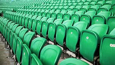 Rows of empty bright green plastic stadium seats seen from an angle.