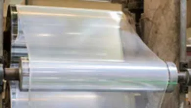 Close-up of clear plastic film passing through industrial metal rollers.