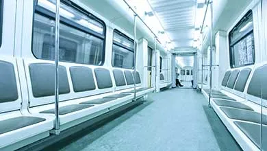 Interior of a brightly lit, modern subway car with empty gray seats along both walls and a central aisle.