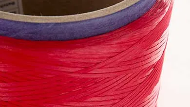 Close-up of a spool of bright red flat twine wound diagonally around a cardboard core, with a purple band at the top.