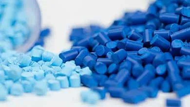 Close-up of light blue plastic pellets spilling from a container beside a pile of dark blue pellets.