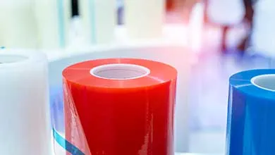 Close-up of large vertical rolls of glossy red, blue, and white plastic film.