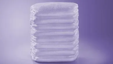 A neatly stacked pile of folded white adult diapers on a purple background.